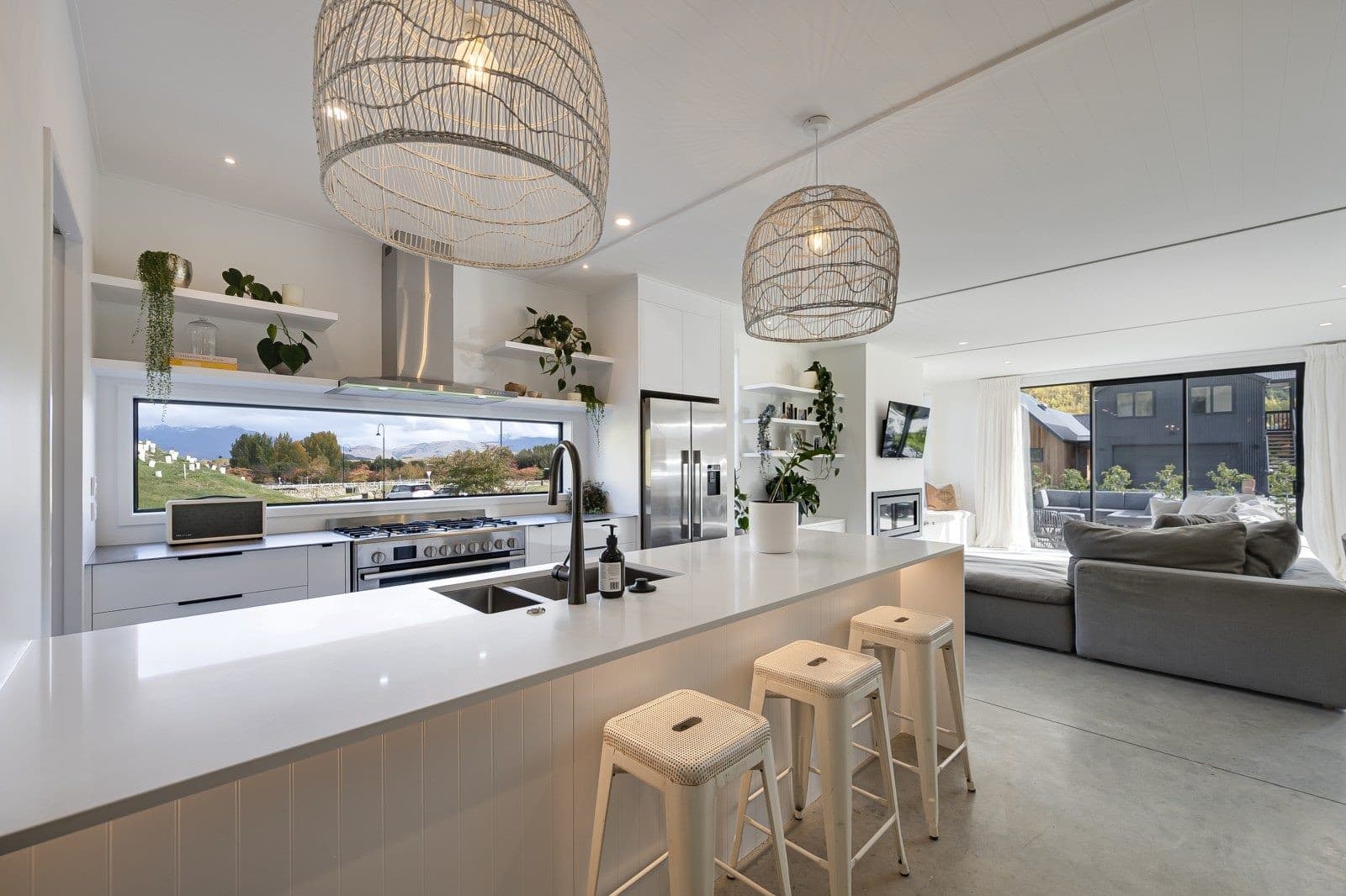 White kitchen with a long island, woven pendant shades and a window strip facing the hills