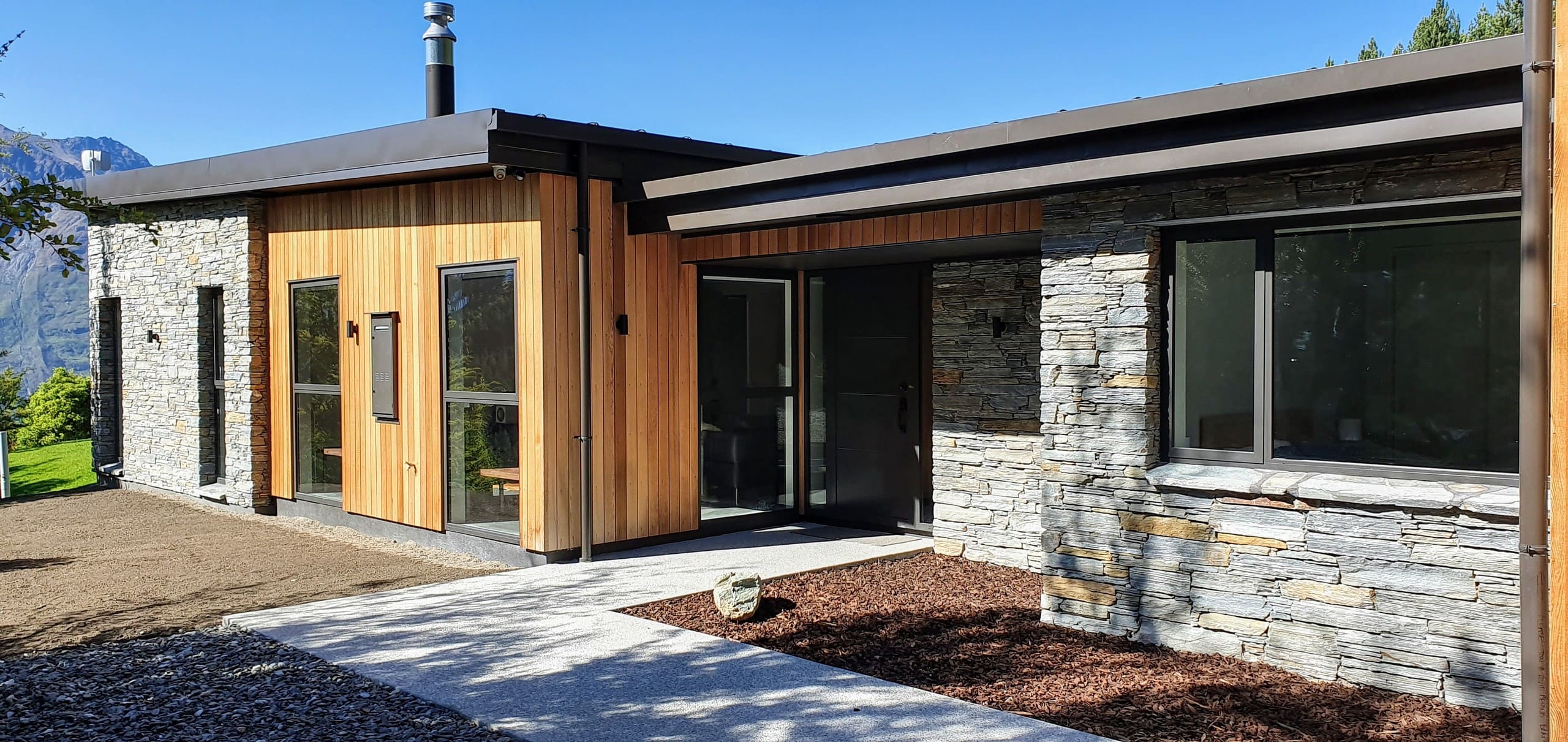 The entrance side in timber and stone, with a long window to the living space