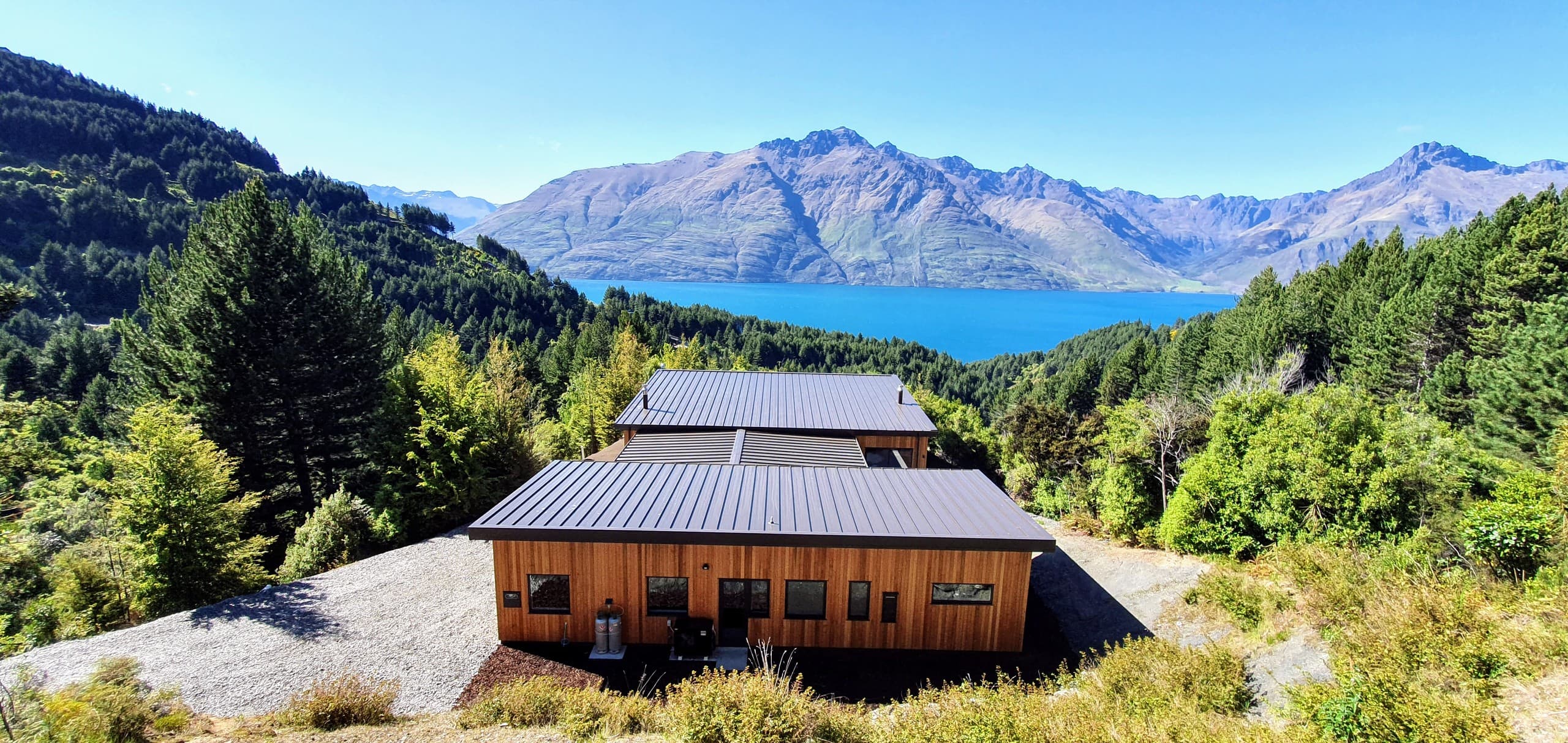 The home seen from above the road, low against the bush with the lake beyond