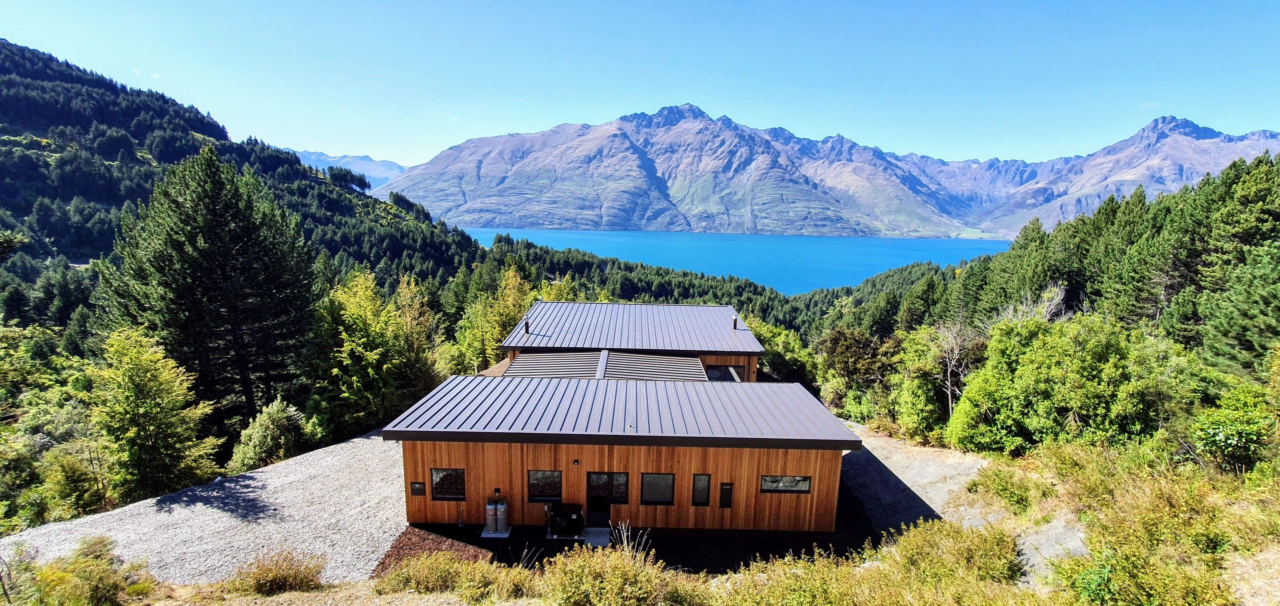 The home seen from above the road, low against the bush with the lake beyond