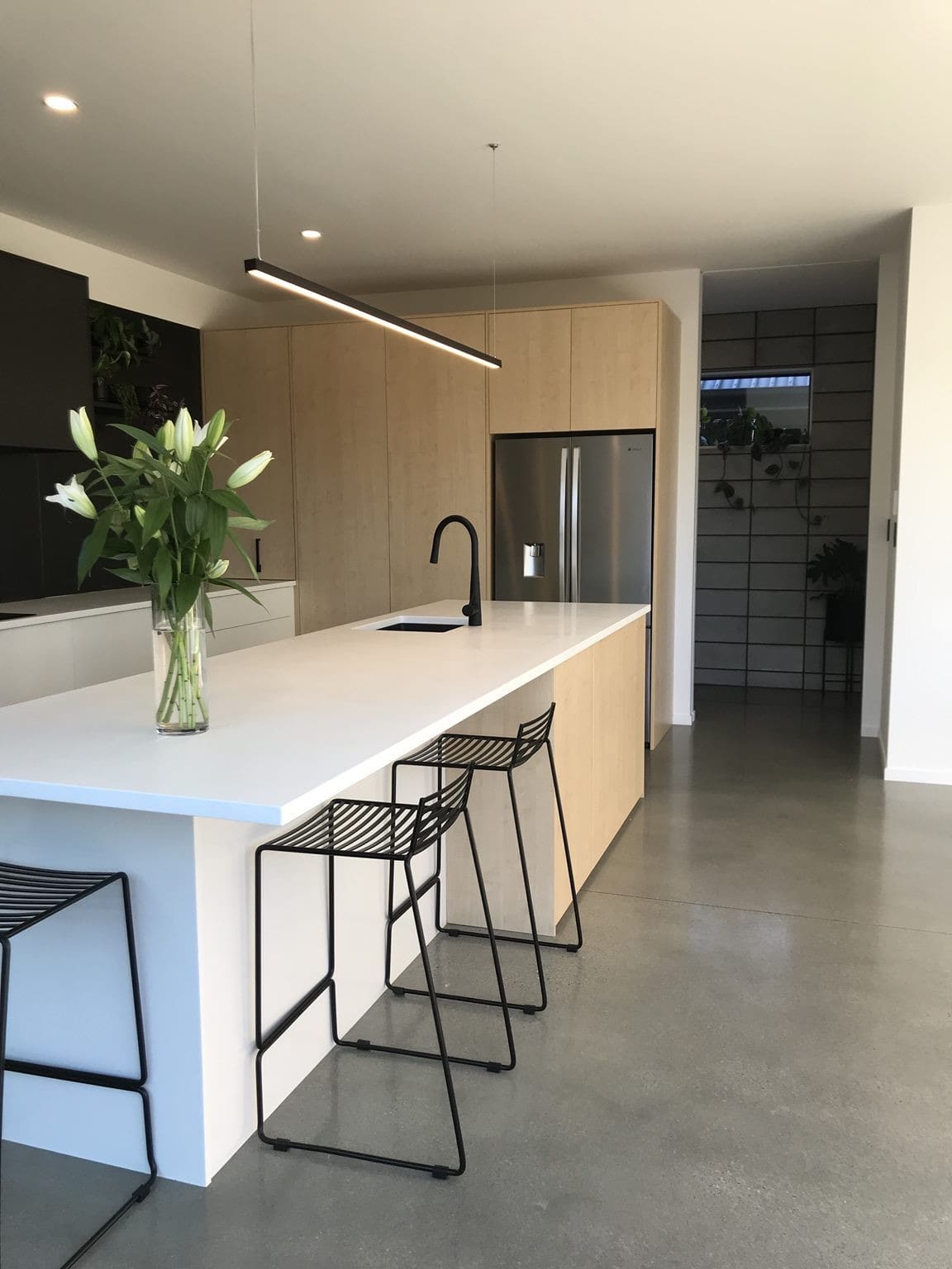 Kitchen with a white island and black stools, flowers on the bench