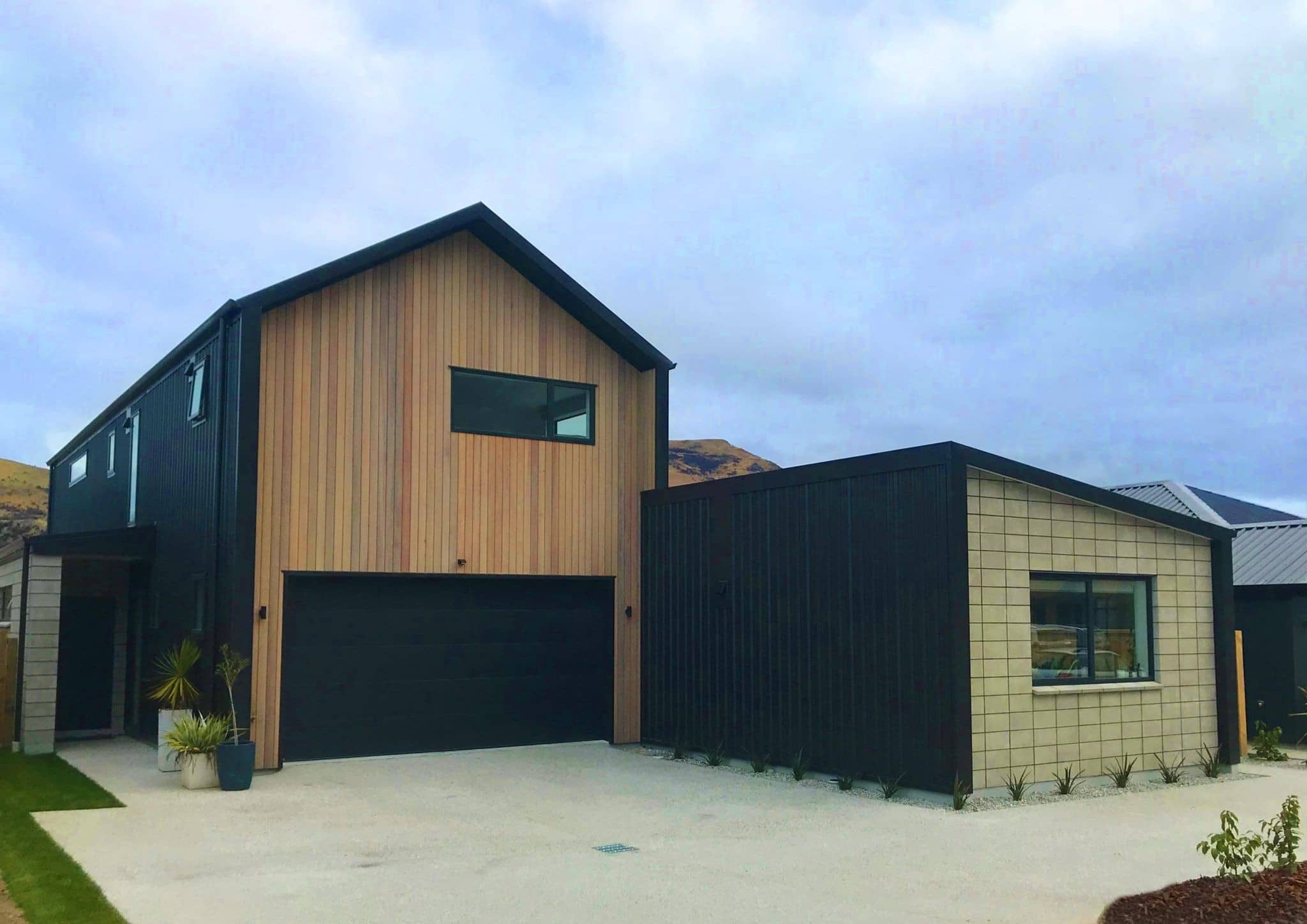 Timber-clad gable above a black garage door, with a single-storey wing running along the driveway
