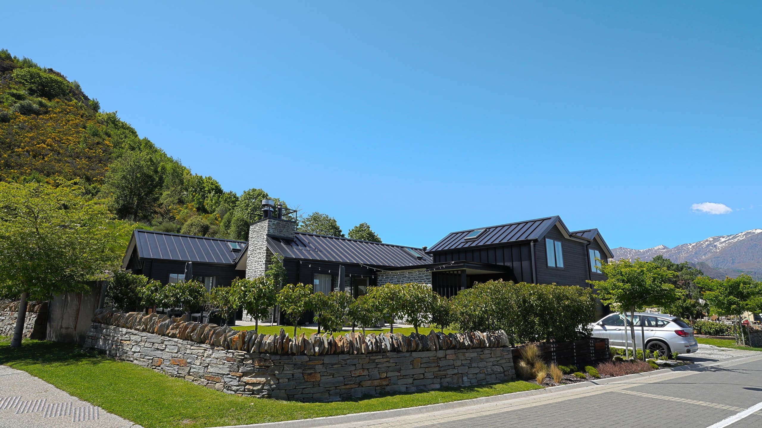 Dark gabled home behind a stone wall, with the hills rising behind it