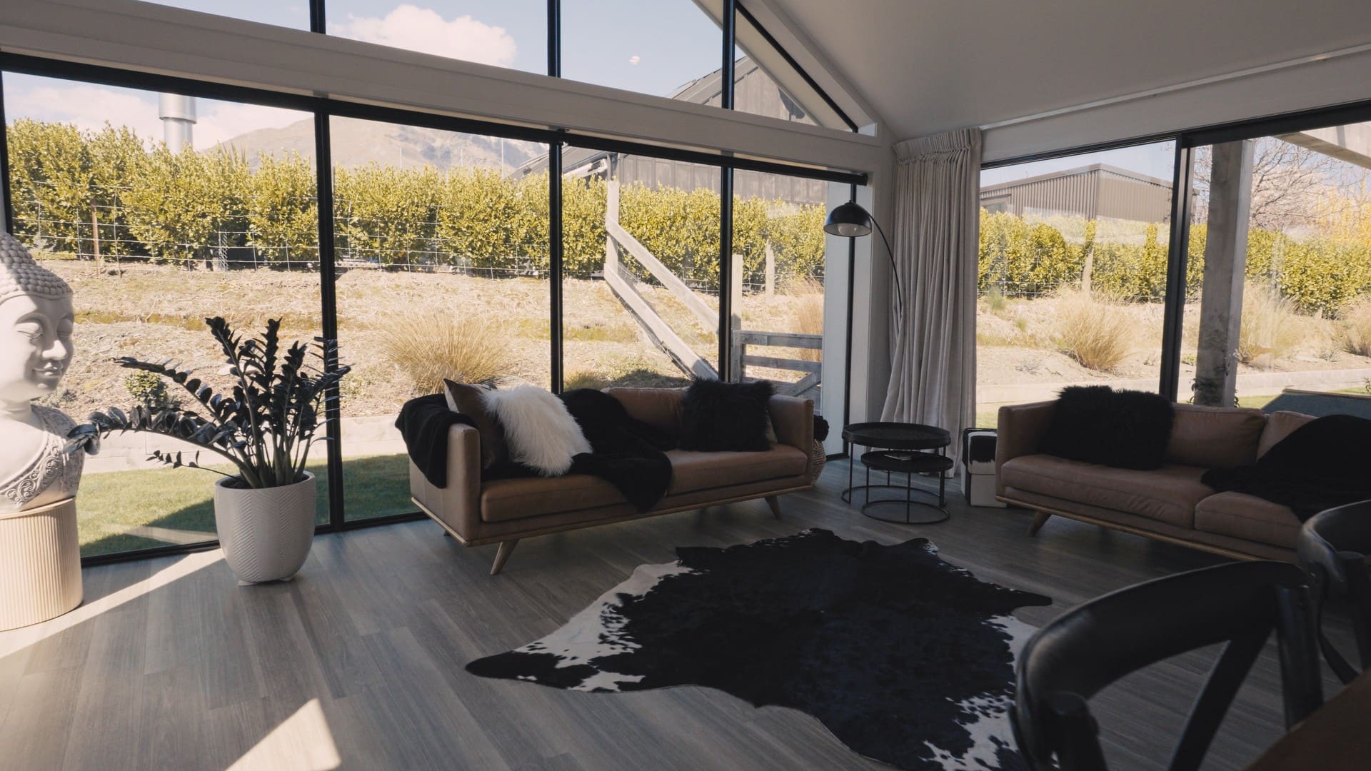 Living room opening through full-height glazing to planted grasses, with a hide rug on the floor