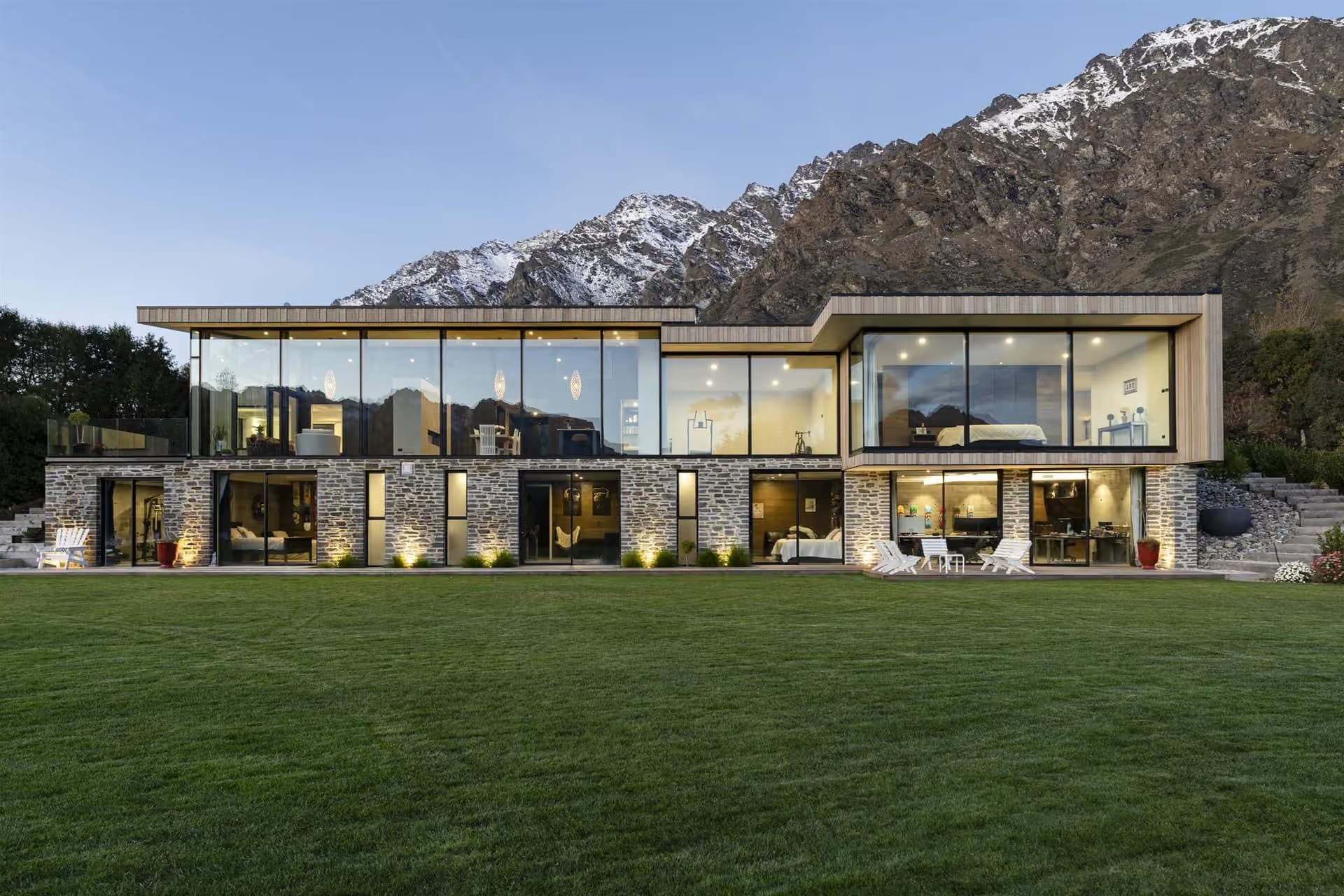 Long glazed elevation facing a lawn, with snow on the Remarkables mountain range behind