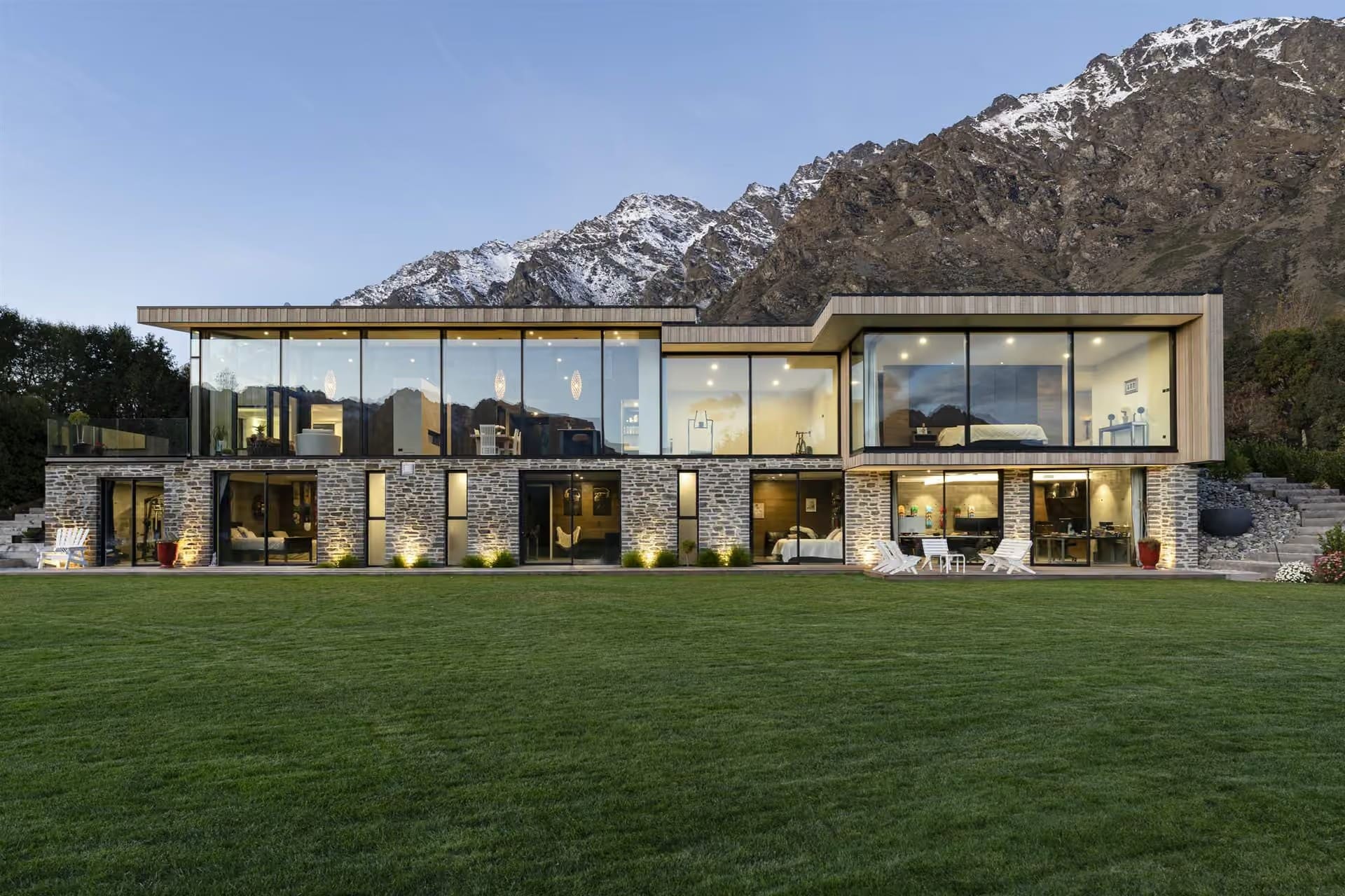 Long glazed elevation facing a lawn, with snow on the Remarkables mountain range behind